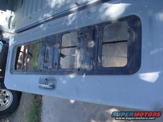Tailgate interior of a light blue 1978 Ford Bronco with a removed window frame and visible latch mechanism