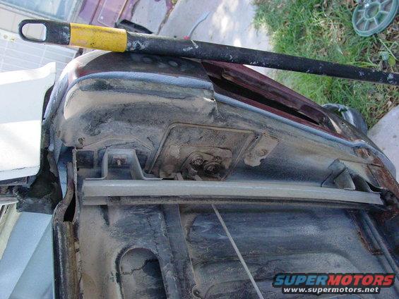 Close-up of a rusty vehicle fender and hood hinge area with a yellow-tipped bar resting on top