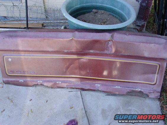 Damaged maroon car door panel with gold trim and visible rust along the bottom edge