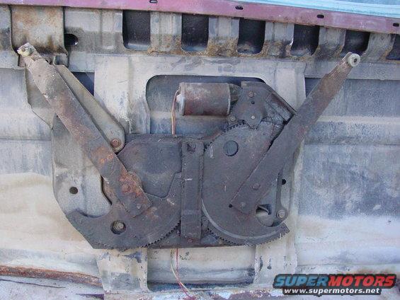 Rusty window regulator mechanism with motor and gears, attached to a red vehicle door interior