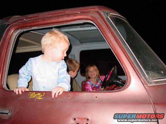 Red Ford Bronco interior with three children visible through the open driver's side window; one child is in the driver's seat