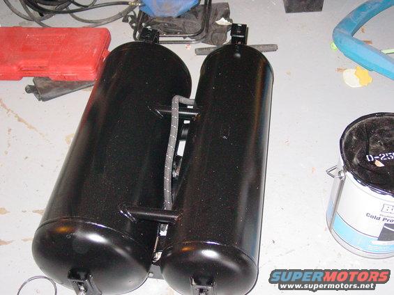 Two black propane tanks connected by hoses and brackets