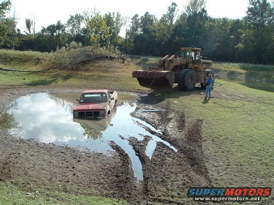 Red pickup truck stuck in mud pit, front loader nearby