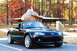 2006 Mazda Miata - A black 2006 Mazda Miata convertible is parked outdoors with a jet and colorful trees in the background.