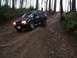 1995 Ford Bronco - A dark blue SUV navigates a challenging muddy path through a dense forest.