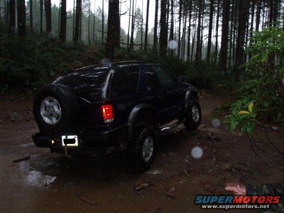 Black SUV with spare tire on back driving on muddy forest trail