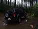 1995 Ford Bronco - A dark-colored SUV navigates a wet, muddy path through a dense forest with tall trees.