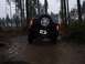 1995 Ford Bronco - A dark blue SUV navigates a muddy path through a dense forest, its spare tire mounted prominently on the rear.