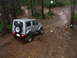 1995 Ford Bronco - Suzuki Samurai navigates a challenging, wet, and muddy off-road path through a wooded area.