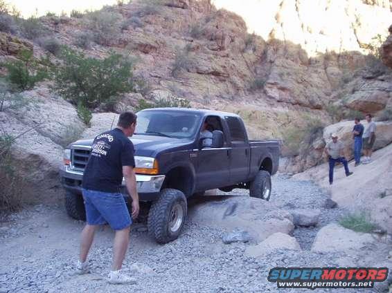 Black Ford F-250 pickup truck on rocky trail with man standing nearby
