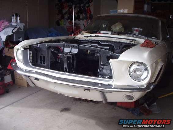 White 1967 Ford Mustang front end with hood open, showing engine bay. Chrome bumper and grille visible