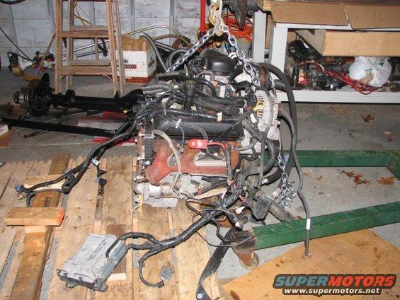 Engine assembly suspended by chains, with wiring harness and ECU visible