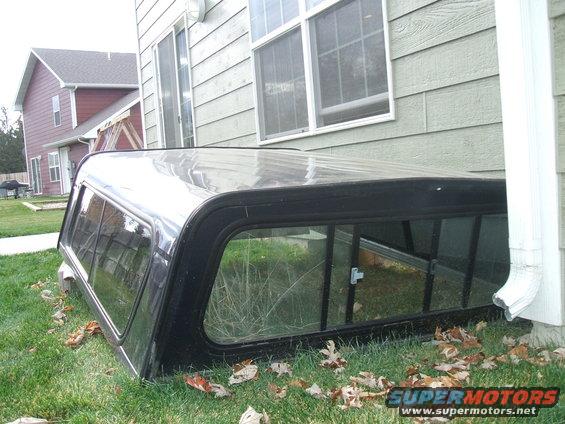 Black truck bed cap with windows, resting on grass