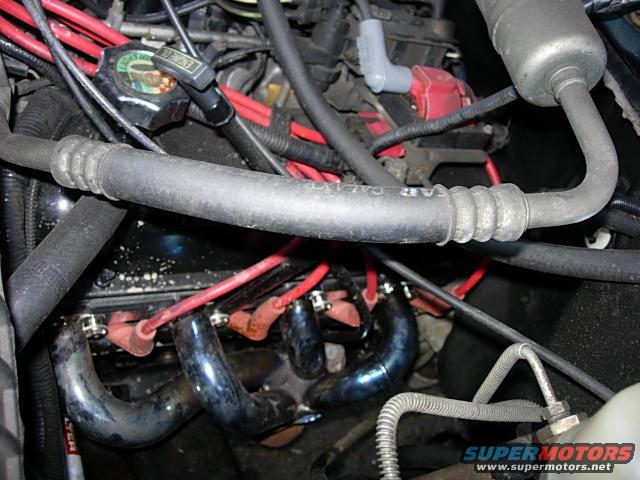 Engine bay with red spark plug wires, blue exhaust manifolds, and a coolant reservoir