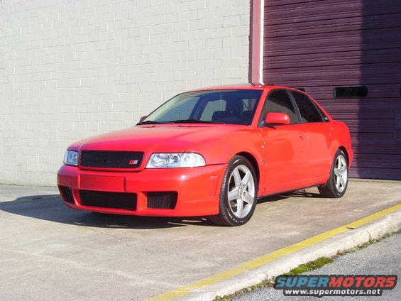 Red 1997 Audi A4 sedan, front 3/4 view, parked on concrete with a brick wall and garage door behind