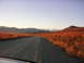 1982 Chevrolet C/K Pickup - A gravel road winds through a landscape of autumn foliage towards snow-capped mountains under a clear sky.