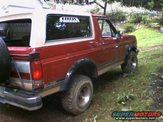 Red and tan Ford Bronco parked on a grassy, muddy area