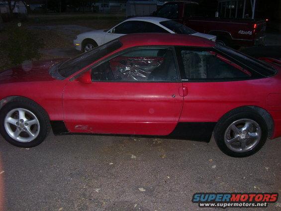 1993 Mazda MX-6 coupe, side view, red with black trim. White car and red truck in background