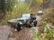 1990 Ford Bronco - Two off-road vehicles traverse a challenging, wet, and rocky trail during autumn.