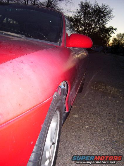 Red sports coupe, front quarter panel and side mirror visible. Dusk lighting