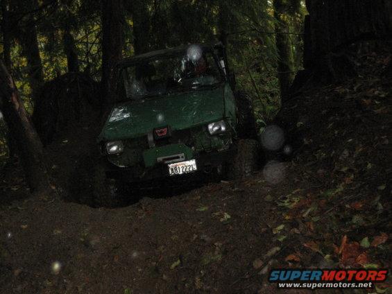 Green off-road vehicle with license plate AB1222L navigating a muddy forest trail