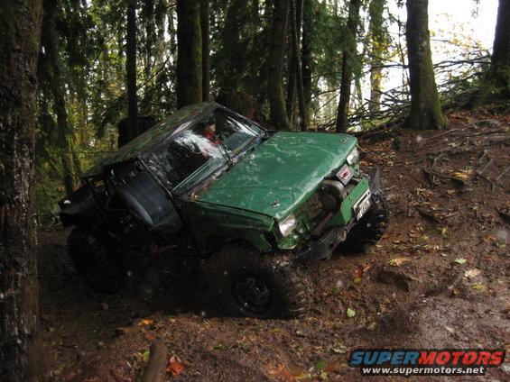 Green off-road vehicle tilted on muddy trail in forest