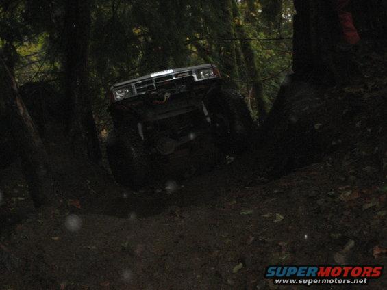1990 Ford Bronco climbing a muddy hill in a forest