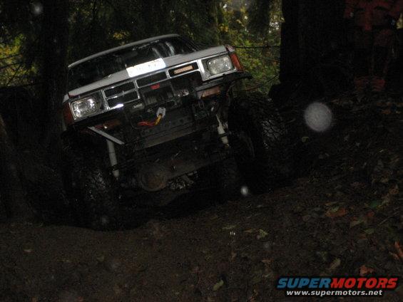 White off-road truck with large tires driving on a muddy trail in the woods