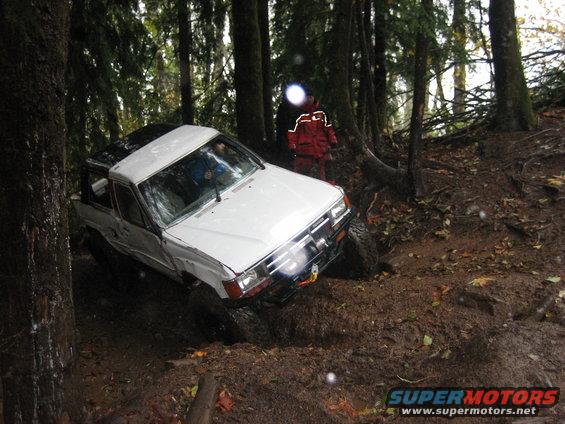White pickup truck with dented fender stuck in mud, front 3/4 view