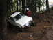 1990 Ford Bronco - A white pickup truck navigates a muddy, wooded trail, its front wheel deep in the mire.