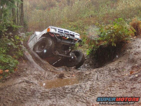 White off-road SUV climbing a muddy hill, front grille and bumper visible