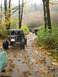 1990 Ford Bronco - Multiple off-road vehicles navigate a wet, wooded trail during autumn.