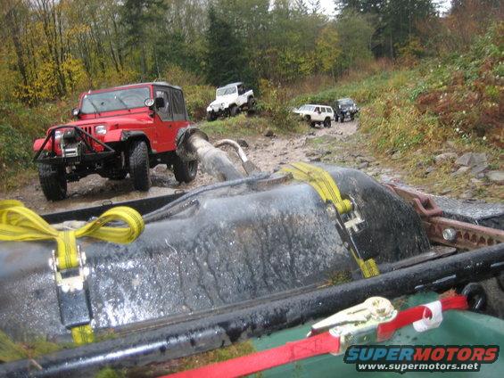 Red Jeep Wrangler with winch on muddy trail, other Jeeps behind