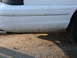 1997 Mercury Grand Marquis - Close-up of a dirty white car bumper and tire, showing the lower body panel and wheel.