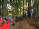 1990 Ford Bronco - Two off-road vehicles navigate a challenging muddy path through a dense forest with onlookers.