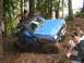 1990 Ford Bronco - A blue off-road vehicle navigates a muddy trail with spectators watching.
