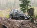 1990 Ford Bronco - Off-roading Jeep Wrangler navigating a muddy incline with a large tree stump nearby.