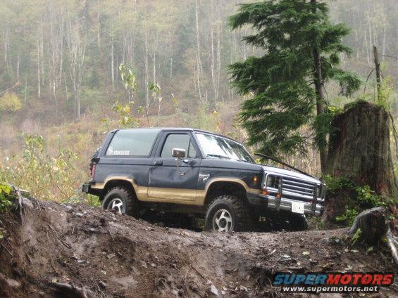 Dark blue and tan Ford Bronco II off-roading on a muddy hill