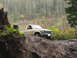 1990 Ford Bronco - A tan pickup truck navigates a steep, muddy incline in a wooded area.