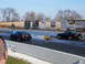 1997 Mercury Grand Marquis - Two black muscle cars compete on a drag strip, with various sponsor signs lining the track.