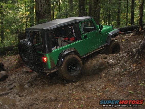Green Jeep Wrangler with a soft top navigating a muddy off-road trail