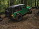 1990 Ford Bronco - Green Jeep Wrangler tackling a challenging muddy trail in a forest setting.