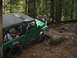 1990 Ford Bronco - A group of people watch as a green Jeep Wrangler navigates a muddy off-road trail.