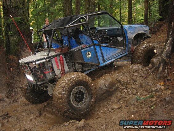 Modified off-road buggy with roll cage stuck in mud on a wooded trail