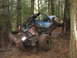 1990 Ford Bronco - Off-road buggy navigating a muddy trail in a forest, leaning heavily against a tree.