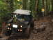 1990 Ford Bronco - This heavily modified off-road vehicle navigates a challenging, muddy path through a dense forest.