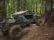 1990 Ford Bronco - This heavily modified off-road vehicle navigates a challenging muddy terrain with onlookers observing.
