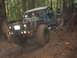 1990 Ford Bronco - This heavily modified off-road vehicle is stuck deep in the mud on a forest trail.