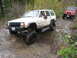 1990 Ford Bronco - A white Jeep Cherokee navigates a challenging rocky path, with a red Jeep Wrangler in the background.
