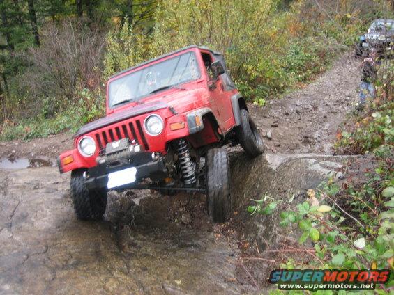 Red Jeep Wrangler navigating a rocky, wet trail with another vehicle behind